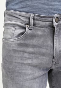 Grå denimjeans med en lätt blekt textur, utrustade med standardfickor, en metallknapp och en märkestagg nära midjan.