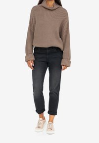 Beige stickad tröja med krage, kombinerad med smala svarta jeans. Modellen har på sig ljusrosa sneakers som visar vikta ärmar och en avslappnad passform.