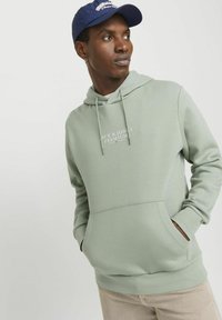 Svetlozelená mikina s kapucňou, predným vreckom a šnúrkami. Na hrudi je potlač "JACK & JONES PREMIUM".