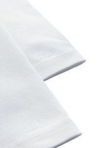 Tessuto di cotone bianco con una texture liscia, caratterizzato da bordi cuciti e dal nome del marchio "Clarks" ricamato in un finish tonale sottile.
