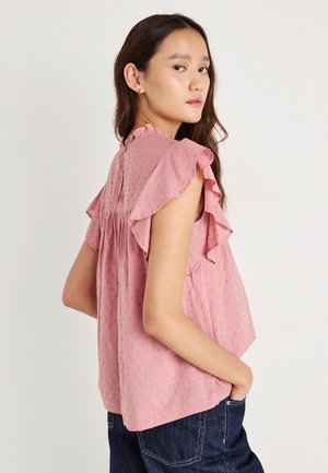 Rosa, teksturert bluse med volanger på ermene, nøkkelhull bak og samlet detalj. Kombinert med mørke denimjeans.