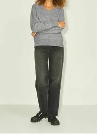 Grauer Strickpullover mit V-Ausschnitt, kombiniert mit schwarzen geraden Jeans und schwarzen Sneakers. Der Pullover hat gerippte Bündchen und einen gerippten Saum.