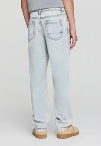 Jeans in denim blu chiaro con una vestibilità rilassata, gambe dritte e due tasche posteriori. Presentano una texture sbiadita e un leggero effetto usurato.