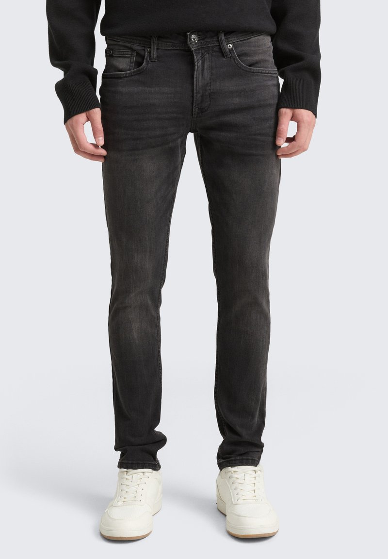 Jeans de denim preto com um corte ajustado, apresentando cinco bolsos, fecho de zip e um desbotado subtil. Combinados com ténis brancos.