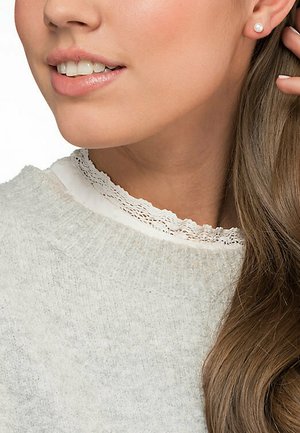 Hellgrauer Pullover mit gerippter Textur und weißem Spitzenkragen. Model trägt einen kleinen Perlenohrring, zeigt glatte Haut und lange Haare.