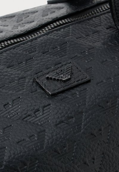 Zwarte faux leren tas met gegraveerde logo patronen. Voorzien van een ritsluiting, gestructureerd oppervlak en een verhoogd logopatch aan de voorkant.
