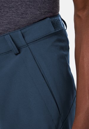 Donkerblauwe broek met verstelbare klittenband tailleband, gedragen door een persoon met een donker gemêleerd shirt, close-up van de taille en zijzak.