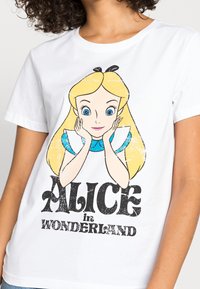 Valkoinen puuvillainen t-paita, jossa on keskeinen graafinen kuva sarjakuvatyttöstä, jolla on vaaleat hiukset, siniset silmät ja päässä panta, sekä teksti "ALICE in WONDERLAND".