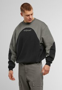 Sudadera con cuello redondo en gris y negro. Presenta un logotipo en el pecho, mangas raglán y un diseño de corte holgado. Está hecha de una tela suave.
