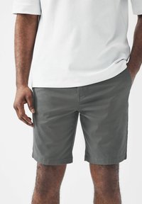 Pantalones cortos de algodón gris con una textura suave, que cuentan con bolsillos laterales y un corte recto, combinados con una camisa blanca de manga corta.