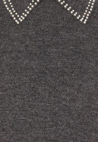 Grå tröja med texturerad tyg, med en krage prydd med små, vita, pärlliknande nitar längs kanterna.