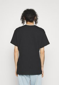 Svart bomullströja med avslappnad passform, korta ärmar och rund halsringning, med synliga sömmar och en slät textur.