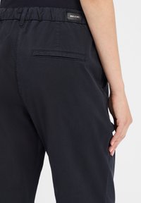 Marineblauwe broek met een zachte textuur, elastische tailleband en een achterzak. Bevat een merketiket op de tailleband.