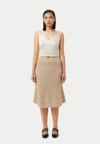 Ljust beige stickad kjol med en utsvängd form och en texturerad mönstring, matchad med en vit satinlinne. Svarta Mary Jane-skor fulländar looken.