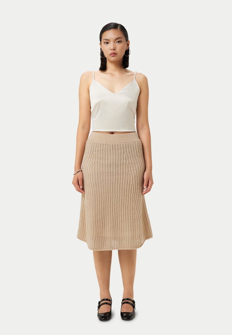 Ljust beige stickad kjol med en utsvängd form och en texturerad mönstring, matchad med en vit satinlinne. Svarta Mary Jane-skor fulländar looken.