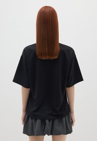 Top negro de manga corta hecho de tejido texturizado, combinado con una falda gris plisada. Enfoque en un diseño sencillo y una silueta casual.