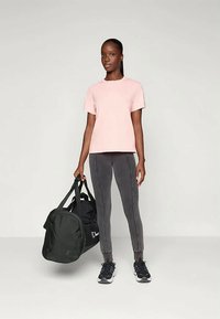 Ljusrosa kortärmad t-shirt, grå leggings med sidodetaljer och svart sportväska. Modellen har på sig svarta sneakers. Minimalistisk bakgrund.