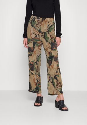 Løse cargobukser med grønt, brunt og beige abstrakt camouflagemønster, stylet med en sort langærmet top og sorte åbne mules med hæl.