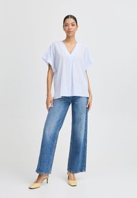 Blusa a righe blu chiaro, con maniche corte e scollatura a V, abbinata a jeans in denim a gamba larga e tacchi color crema. Design semplice e vestibilità morbida.