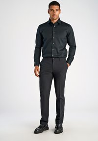 Zwarte, langemouwen button-up shirt met een glanzende afwerking, gecombineerd met donkere broeken en zwarte schoenen. Beschikt over een klassieke kraag en knopen.