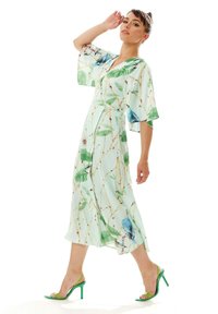 Floral-patterned, light blue dress with short sleeves, V-neck, and waist tie. Worn with green heeled sandals. Smooth, lightweight fabric.