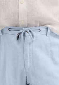 Light blue linen trousers with a drawstring waist, featuring metal eyelets and a braided tie. Smooth texture with stitched seams.