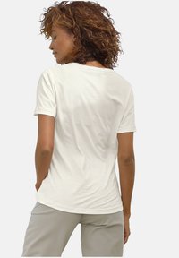 Helles beiges Baumwoll-T-Shirt mit entspannter Passform, kurzen Ärmeln und gerundetem Halsausschnitt. Glatte Textur mit minimalen Nahtdetails auf dem Rücken.