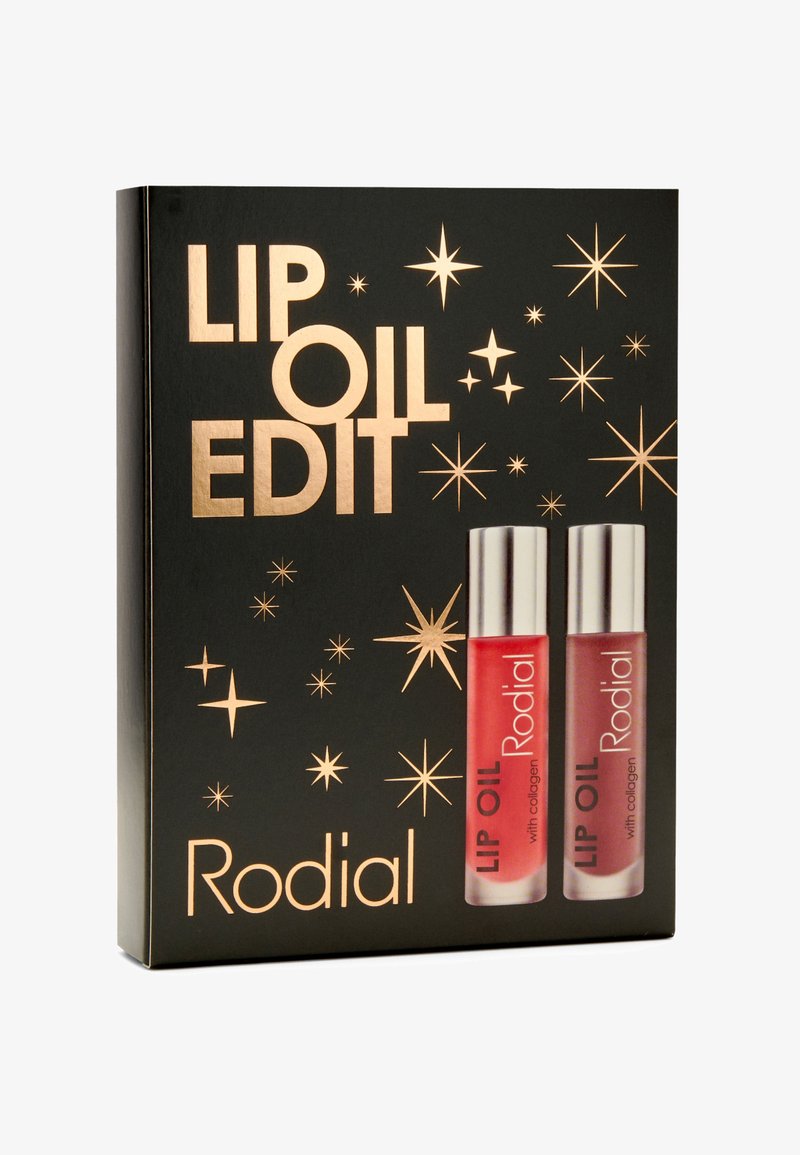 Die Verpackung der Rodial Lip Oil Edit zeigt einen schwarzen Hintergrund mit goldener Schrift und Sternakzenten und präsentiert zwei Lip Oil Tuben – eine rote, eine klare.