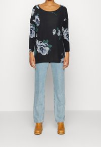 Schwarzes Langarmoberteil mit blauem Blumenmuster, kombiniert mit hellblauen, geraden Jeans und braunen, hohen Stiefeletten.