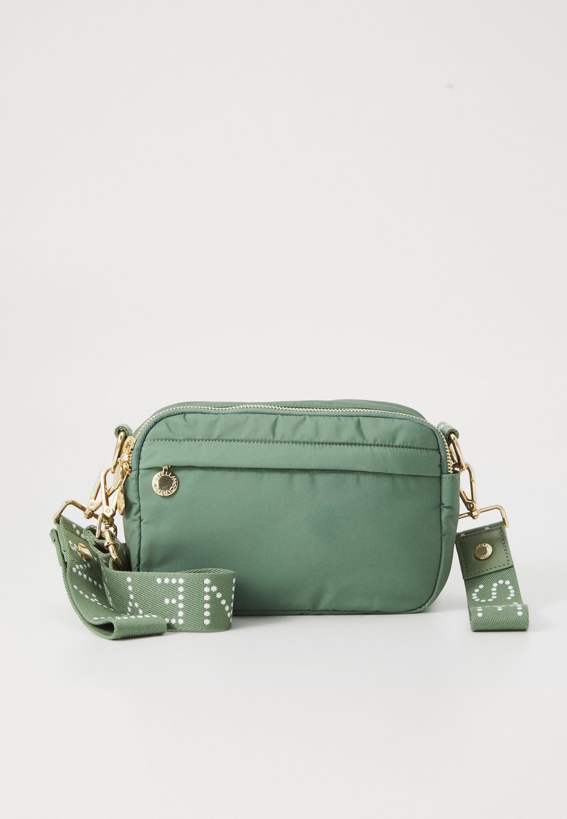 Zaļš neilona plecu soma ar zelta detaļām, ar rāvējslēdzēja aizdari un regulējamu siksnu, kurai ir balti uzraksti. Gluda virsma un taisnstūra forma.