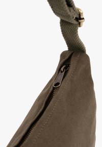 Close-up of a brown fabric bag corner showing a metal zipper pull and part of an adjustable textured strap.