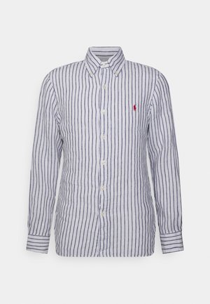 Camisa blanca de manga larga con botones, con rayas verticales azul marino y un pequeño logo bordado en rojo en el pecho izquierdo.