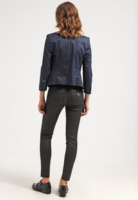 Marinblå kavaj med en skräddarsydd design, i kombination med svarta slim-fit jeans. Outfiten har en mjuk textur och minimala detaljer i metall.