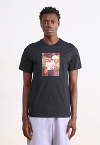 Schwarzes Baumwoll-T-Shirt mit einem zentralen Grafikmotiv eines Basketballspielers. Kurze Ärmel, runder Halsausschnitt, glatte Textur.