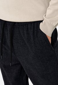 Dark gray jogger pants with a textured fabric, elastic waistband, and adjustable drawstring. Side pockets visible near the waist.