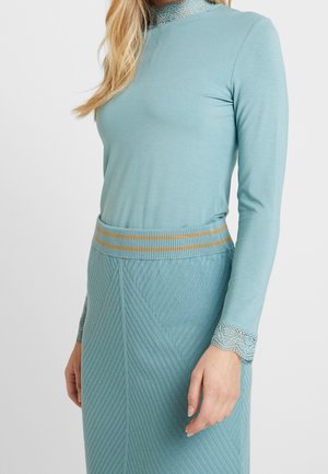 Haut à manches longues bleu clair avec des bordures en dentelle au cou et aux poignets, associé à une jupe crayon texturée avec une taille côtelée et des motifs diagonaux.