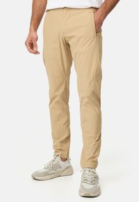 Pantalon beige, fuselé, en tissu léger avec poches latérales. Associé à des baskets de couleur claire avec des détails en maille et en caoutchouc.