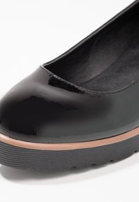 Chaussure en cuir verni noir avec un bout rond, semelle en caoutchouc noir texturé et doublure intérieure lisse. Pas de motifs ni d accents visibles.