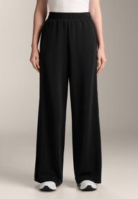 Czarne spodnie o szerokich nogawkach z elastycznym paskiem w talii, wykonane z miękkiego, lekkiego materiału. Mają gładką fakturę i sięgają do kostek.