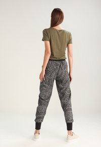 Oliwkowa koszulka z krótkim rękawem połączona z czarnymi dresami w wzory, posiadającymi ściągacze i luźny krój, uzupełniona jasnym obuwiem.