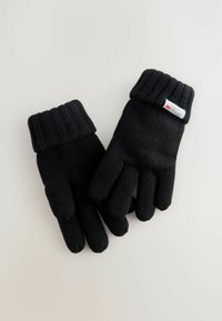 Gants en tricot noirs avec un poignet côtelé. Fabriqués en tissu texturé, présentant des doigts individuels et une petite étiquette sur un gant.