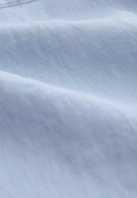 Tissu bleu clair à la texture lisse, présentant un drapé doux et des motifs subtils de tissage, reflétant la lumière en douceur.