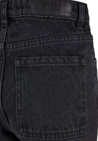 Jeans de denim negro con una textura sólida, bolsillo trasero y una etiqueta de cuero visible con "Urban Classics" grabada en la cintura.
