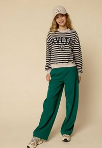 Geribbelde crèmekleurige en marineblauwe sweatshirt met "RVLTN" opdruk, gecombineerd met hoge groene broek en grijze sneakers. Casual, ontspannen pasvorm.