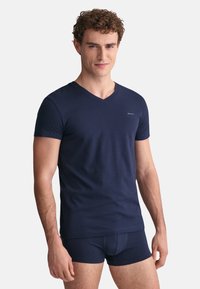 Marineblaue V-Ausschnitt-T-Shirts aus weicher Baumwolle, mit kurzen Ärmeln und einem dezenten Logo auf der Brust. Kombination mit passenden dunklen Shorts.