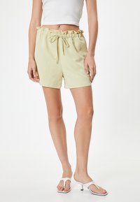 Lys gule shorts med en fløjlsblød elastisk livrem og snøre. Materialet ser glat og blødt ud. Bæres med hvide hæle sandals.