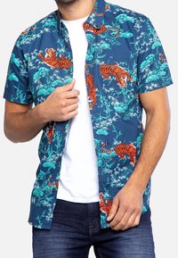 Camisa de manga corta en tejido azul marino con vibrantes patrones de tigres naranjas y follaje en color teal. Cierre de botones en la parte delantera con un corte relajado.