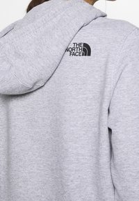 Sudadera gris hecha de una tela suave. Cuenta con un bolsillo canguro en la parte delantera, puños acanalados y un logo negro en la parte posterior. Diseño casual.