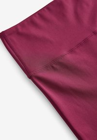 Bordeaux actiewearstof met een gladde, matte textuur. Heeft platte naden langs de randen, wat het rekbare en ademende ontwerp accentueert.