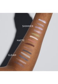 Braccio con campioni cosmetici che mostrano tre categorie: shimmer, opaco e brillante. I colori includono viola, marroni, verdi e metallici.